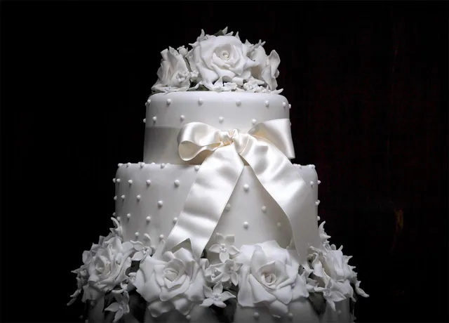 Torta nuziale bianca a due piani con grande fiocco di raso e rose bianche su sfondo nero
