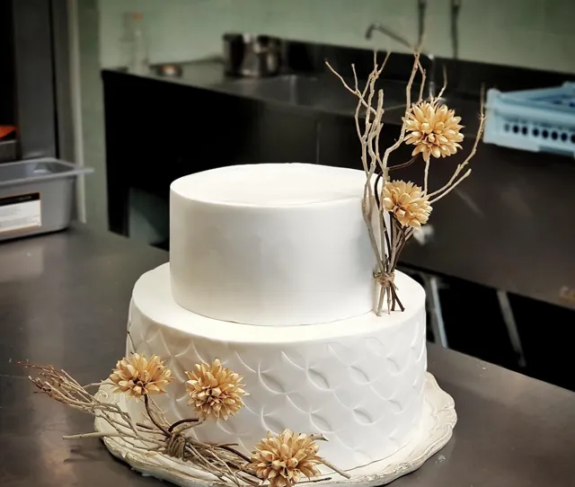 Torta bianca a due piani con motivo a squame in rilievo, rametti secchi e fiori di zucchero dorati