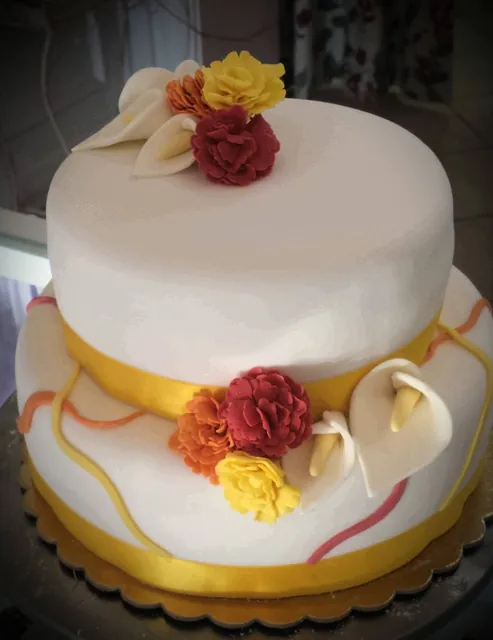 Torta rotonda bianca a due piani con calle, fiori rossi e gialli e nastro dorato