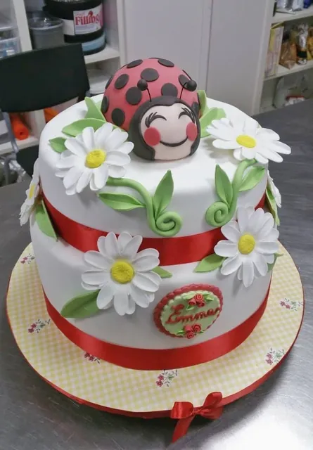 La torta intera con coccinella, margherite e nastro rosso
