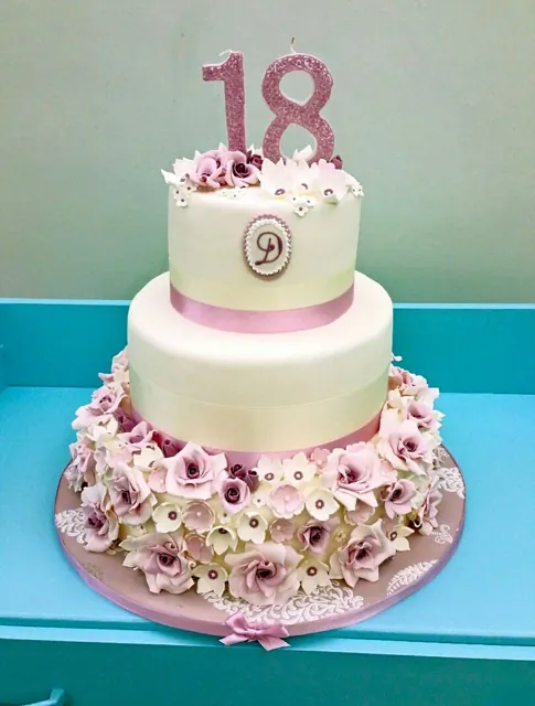 Torta a due piani color crema con base ricoperta di rose rosa in zucchero e grande candela numero 18 glitterata