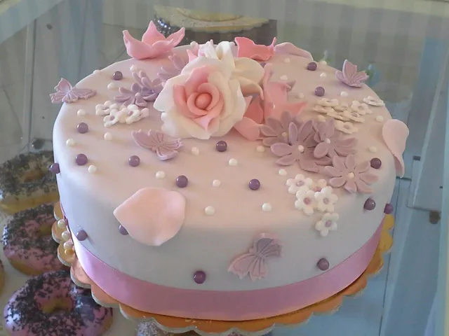 Torta rotonda rosa cipria con rose, petali, perline e farfalle di zucchero