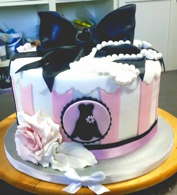 Torta rotonda a righe rosa e bianche con grande fiocco nero, perle e medaglione con abito nero