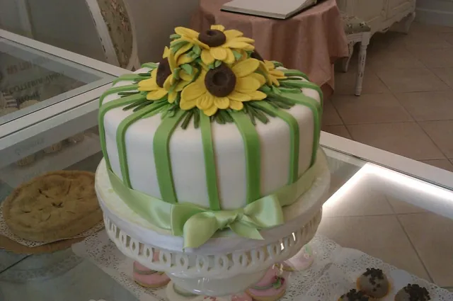 Torta rotonda con righe verdi, fiocco verde e girasoli di zucchero sulla sommità