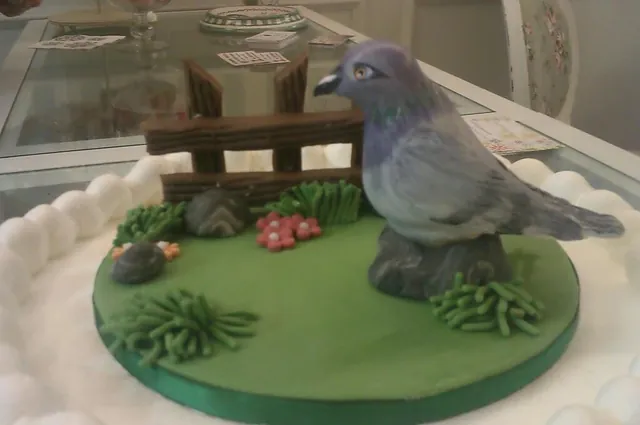 Scultura in pasta di zucchero di un piccione su uno steccato di legno e prato verde