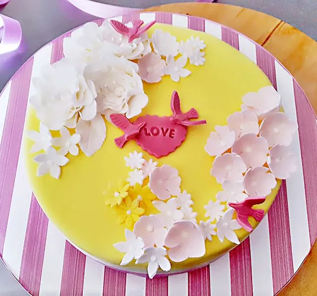 Torta gialla con cuore LOVE, uccellini e fiori bianchi su base a righe rosa