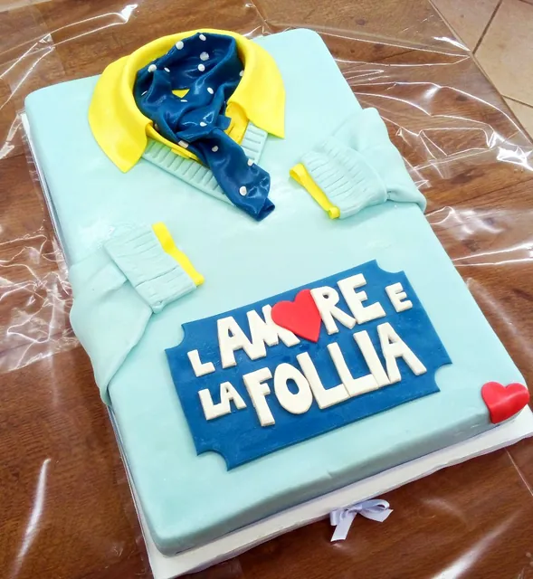 Torta a forma di maglione azzurro con colletto giallo, foulard a pois e targa blu