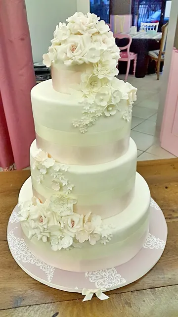 Torta nuziale a quattro piani bianca con nastri rosa cipria e cascata di rose e fiori in zucchero