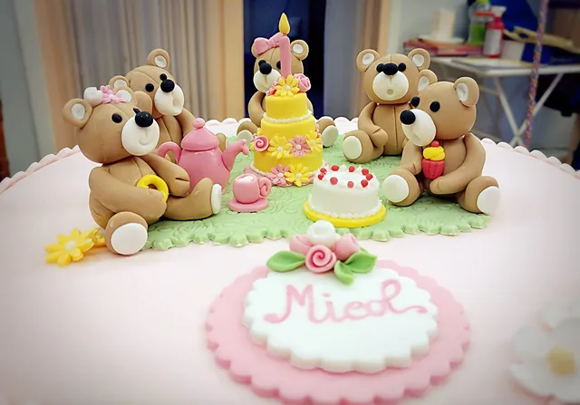 Gruppo di orsetti in pasta di zucchero a un picnic con teiera, cupcake e torta con candelina