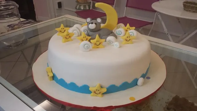 Torta rotonda bianca in pasta di zucchero con orsetto grigio su luna gialla, nuvolette e stelline sorridenti, fascia azzurra