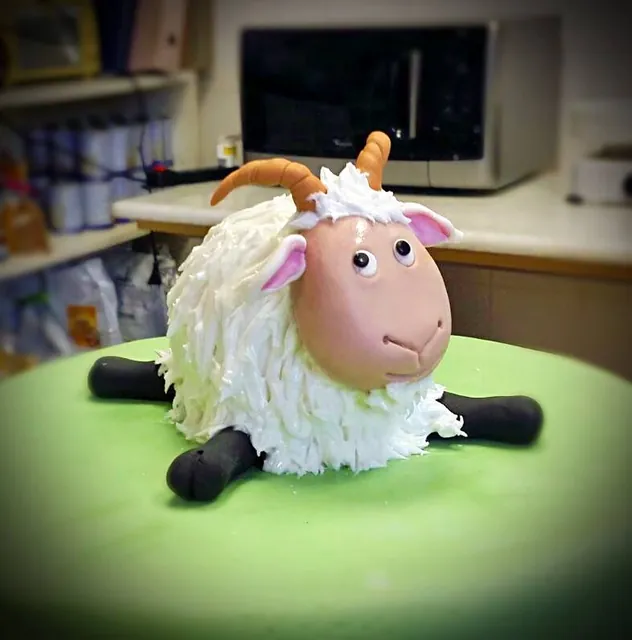 Scultura di pecorella in pasta di zucchero con riccioli bianchi e corna su un prato verde