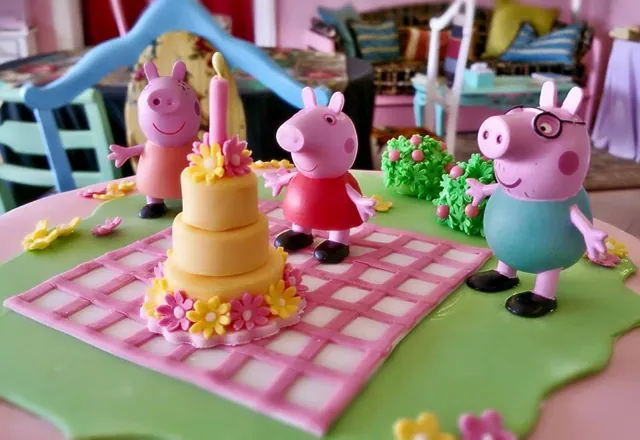 Primo piano di Peppa Pig, George e la famiglia attorno a una piccola torta con candelina su prato di zucchero