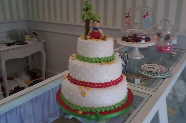 Torta a tre piani bianca con bordi rossi e verdi e statuina di Pinocchio con monete d'oro