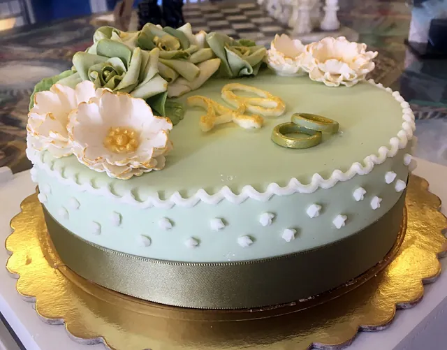 Torta rotonda verde salvia con rose di zucchero, fiori avorio, due fedi dorate e il numero 40