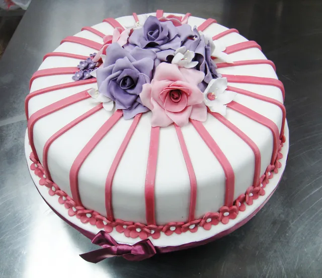 Torta rotonda bianca con righe rosa e un mazzo di rose di zucchero viola e rosa