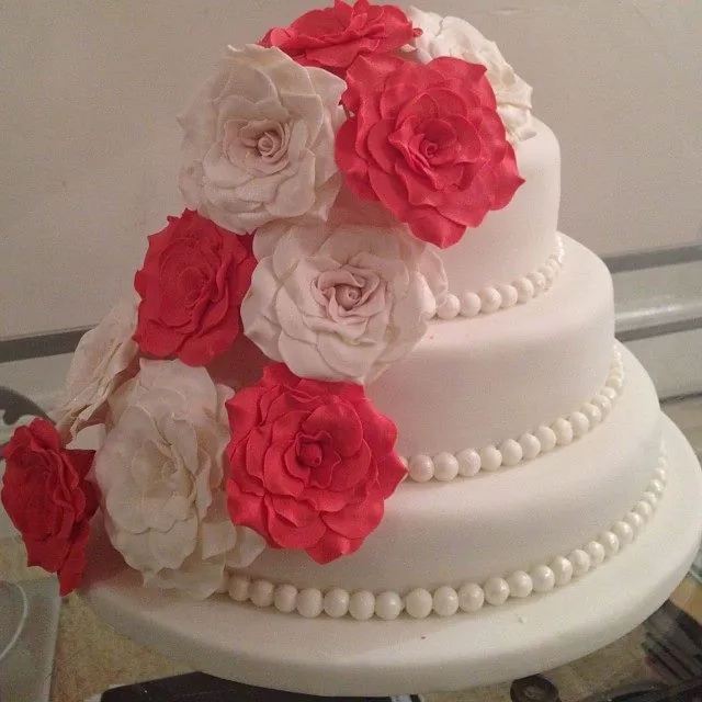 Torta nuziale a tre piani in pasta di zucchero bianca con perline e rose rosse e avorio che scendono a cascata