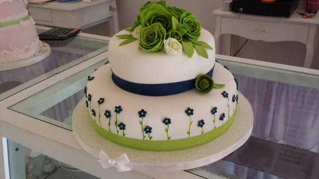 Torta a due piani bianca con rose verdi, nastro blu e fiorellini blu sul bordo