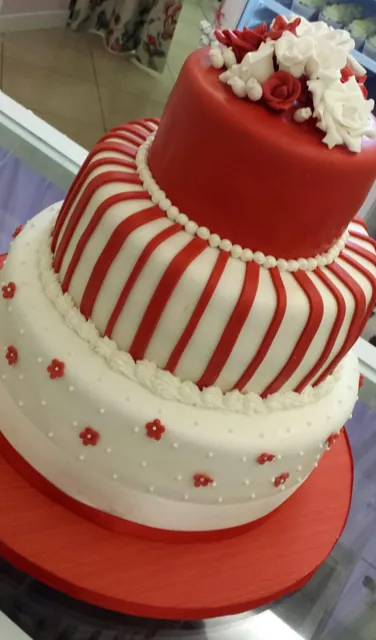 Torta a due piani inclinata con piano rosso a righe, base bianca a fiorellini e rose bianche in cima