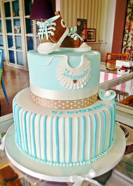 Torta a due piani azzurra a righe con bavaglino e scarpine da neonato in pasta di zucchero