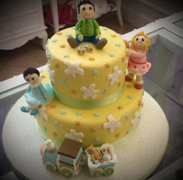 Torta a due piani gialla con stelline, statuine di bambini e trenino con orsetto