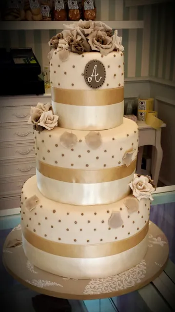Torta nuziale a tre piani avorio e oro con nastri di raso, rose tortora e monogramma