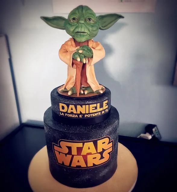 Torta a due piani nera con glitter, logo di Star Wars e statua di Yoda in pasta di zucchero in cima
