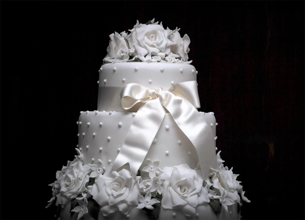 Torta nuziale bianca a due piani con grande fiocco di raso e rose bianche su sfondo nero