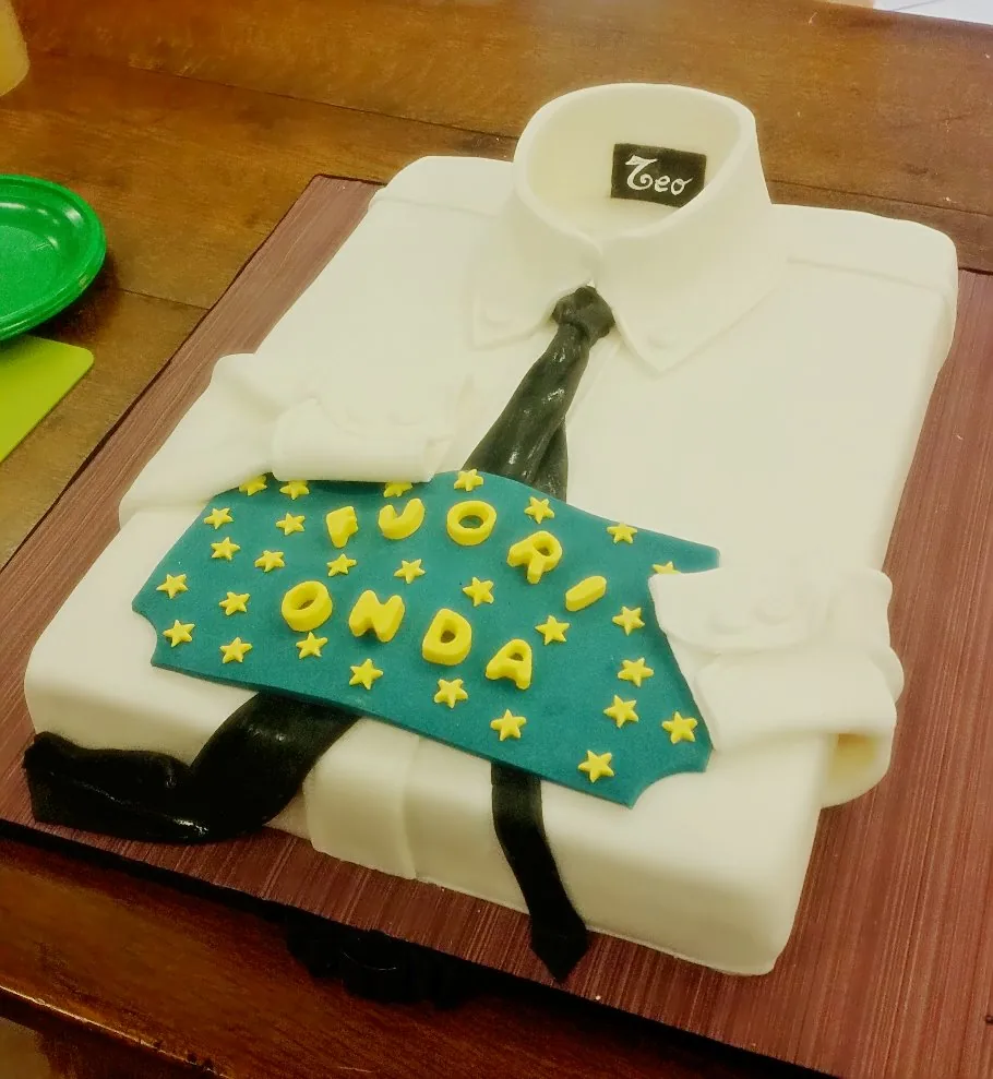 Torta a forma di camicia bianca con cravatta nera e targa blu con stelle gialle