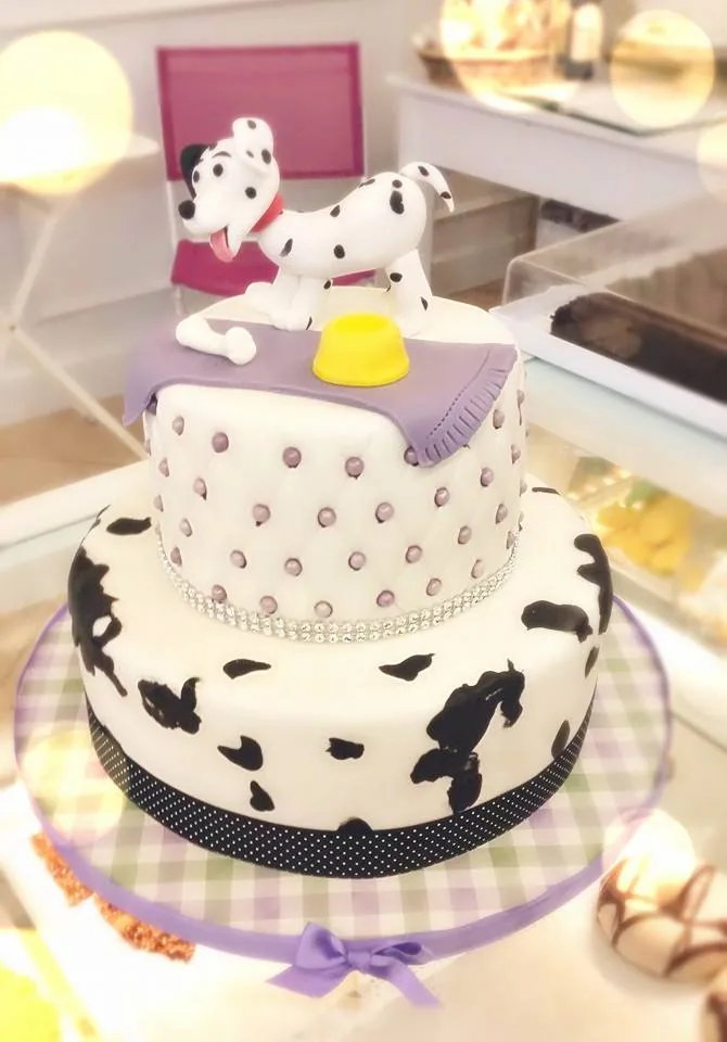 Torta a due piani con macchie da dalmata, bottoni lilla e un cagnolino dalmata in pasta di zucchero sulla cima