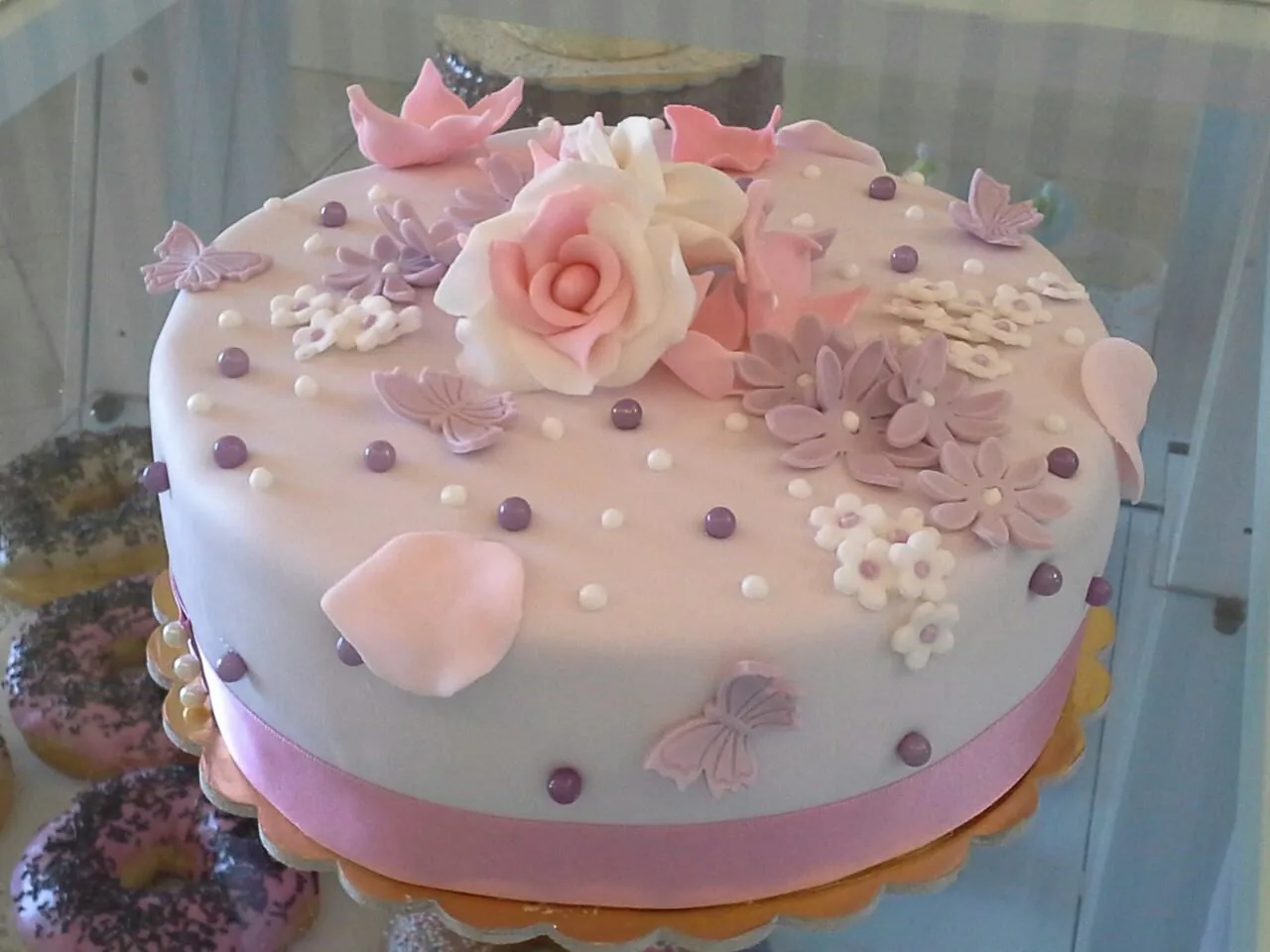 Torta rotonda rosa cipria con rose, petali, perline e farfalle di zucchero