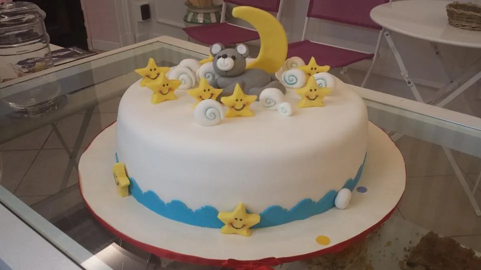 Torta rotonda bianca in pasta di zucchero con orsetto grigio su luna gialla, nuvolette e stelline sorridenti, fascia azzurra