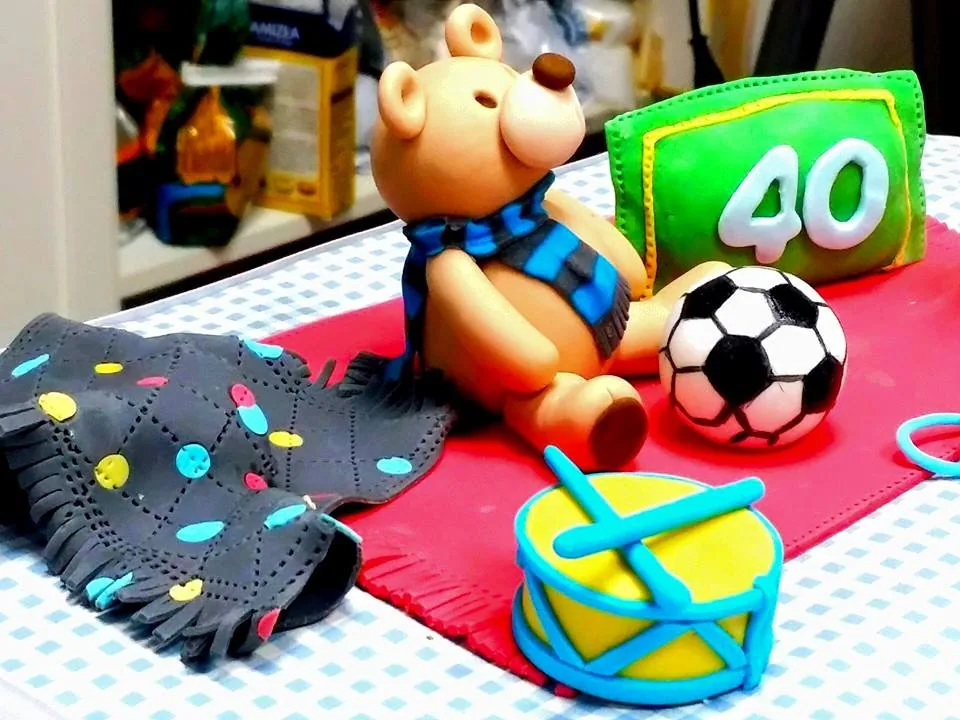Orsetto in zucchero con sciarpa, pallone, tamburello e cuscino con numero 40 su tovaglia a quadretti