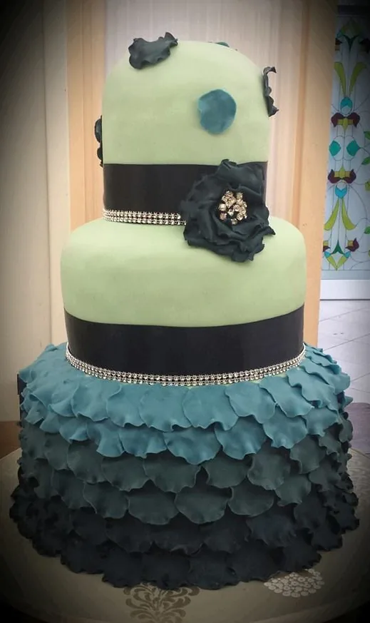 Torta a tre piani con gonna di petali blu, piani verde menta, nastro con brillantini e fiore scuro