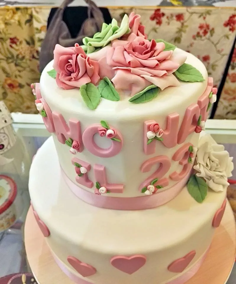 Torta a due piani bianca con cuori rosa, lettere rosa in rilievo e rose di zucchero