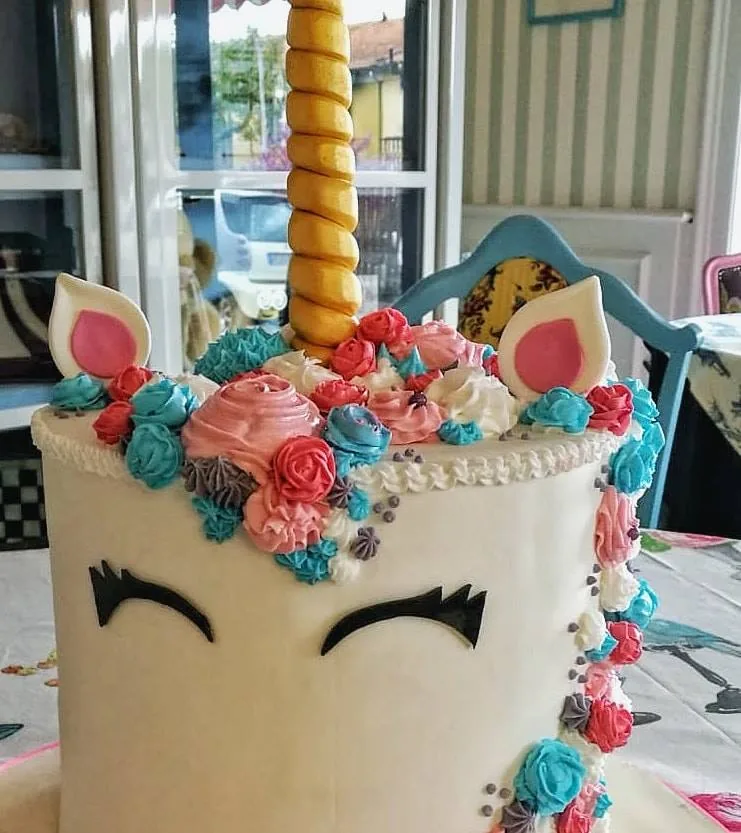 Primo piano della testa di un unicorno di torta con corno dorato, orecchie rosa e roselline di crema